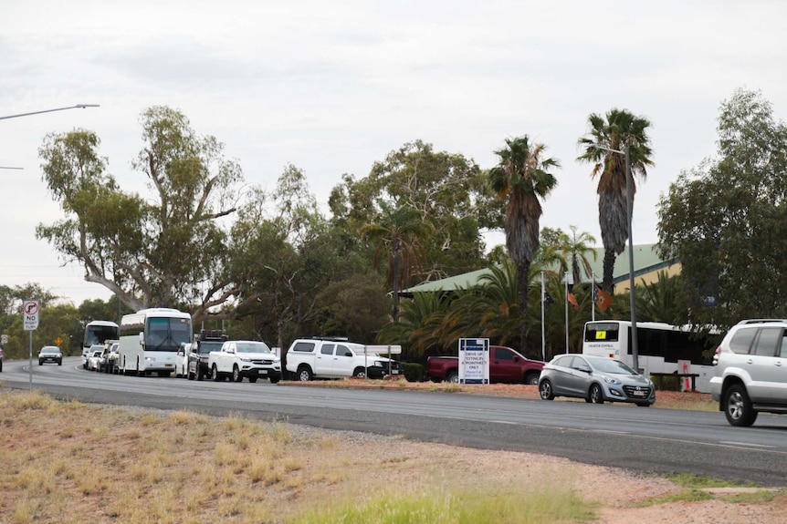 A long line outside the Todd Facility in Alice Springs, cars and a bus can be seen on the street.