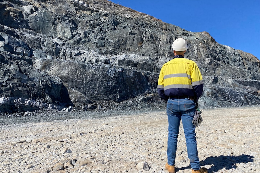 A man wearing a hi-vis jacket stands in front of a pile of rocks.