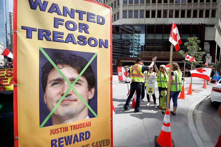 A large portrait sign shows an image of Justin Trudeau with a green x over him and the words 'wanted for treason' above it.