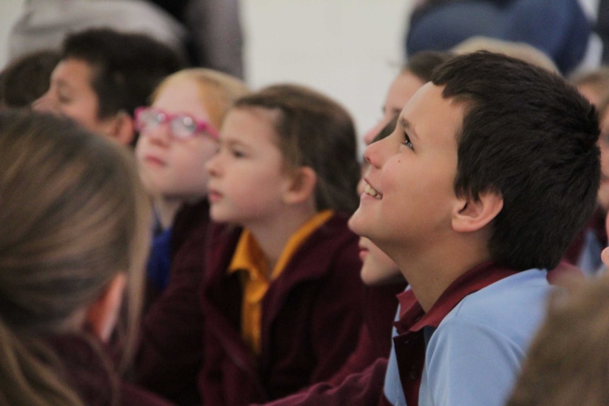 A group of students, one in the middle smiling, watch and listen to a talk.