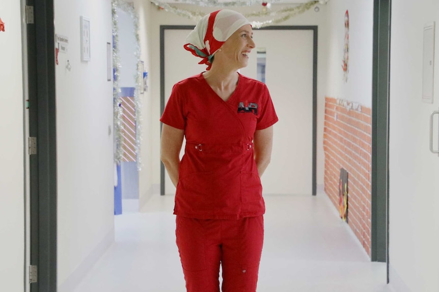 A doctor in red scrubs standing in a hospital hallway and smiling.