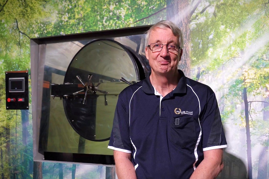 A man with grey hair and glasses stands in front of a cremator.