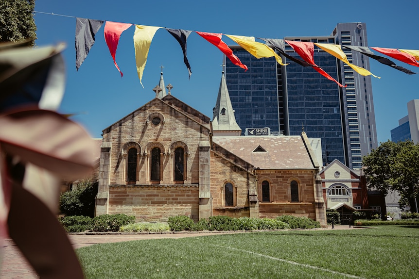 Exterior of a church against a city skyline with a line of bunting in the foreground.