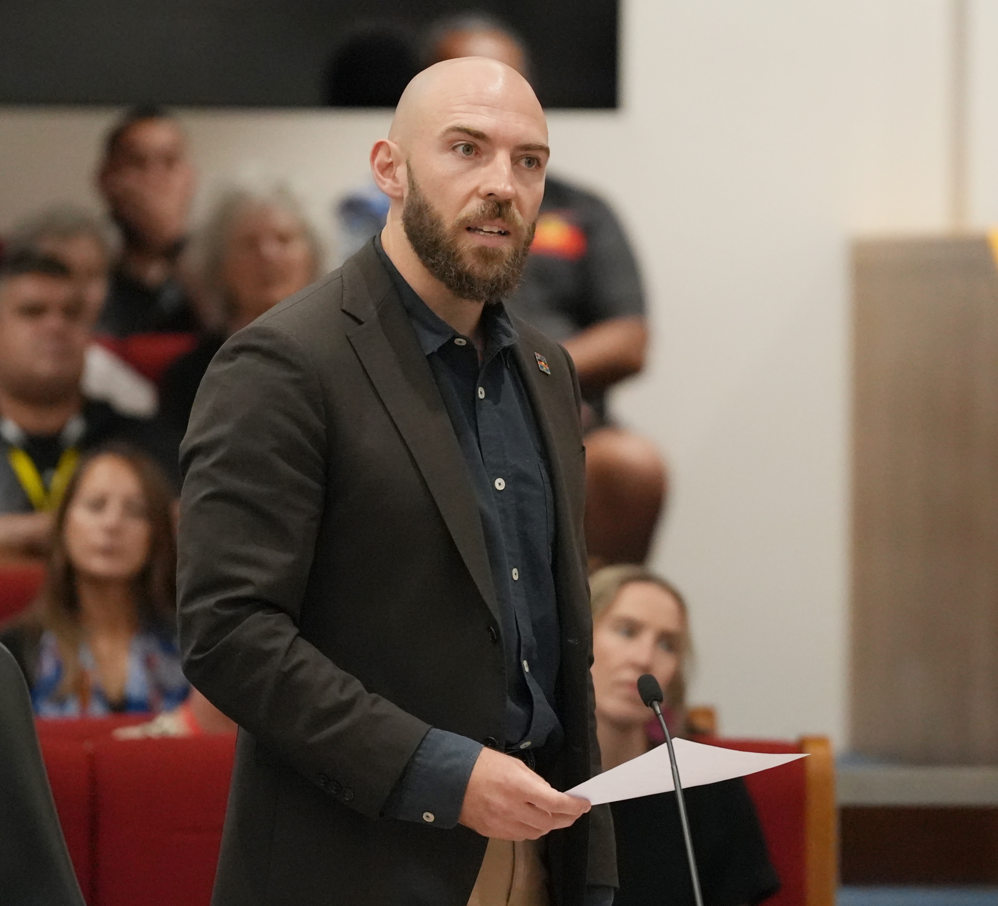 Un hombre calvo con traje se para detrás de un podio y habla con seriedad.