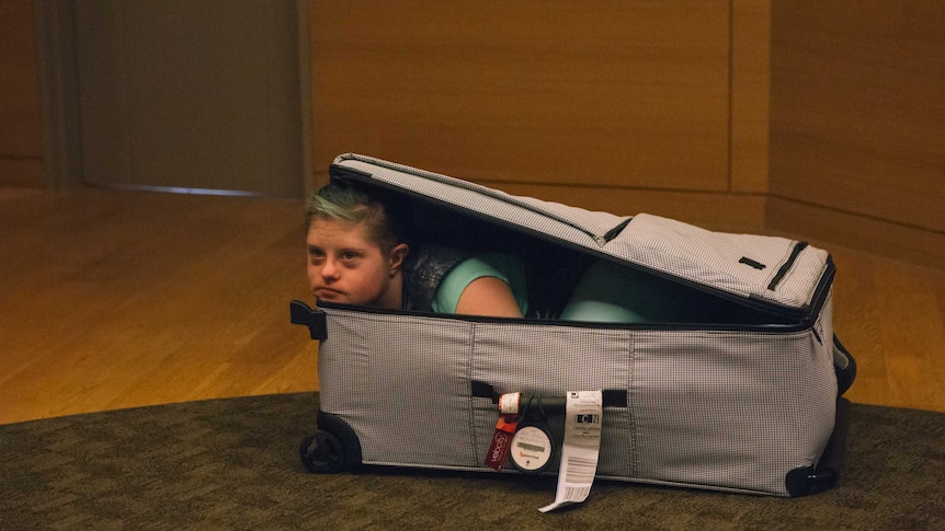 A person looking out from inside an open suitcase.