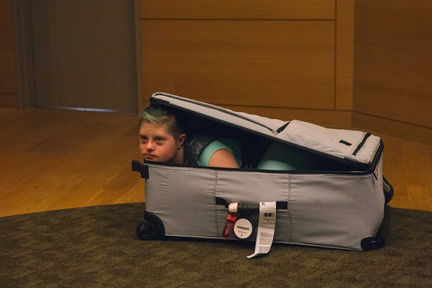 A person looking out from inside an open suitcase.