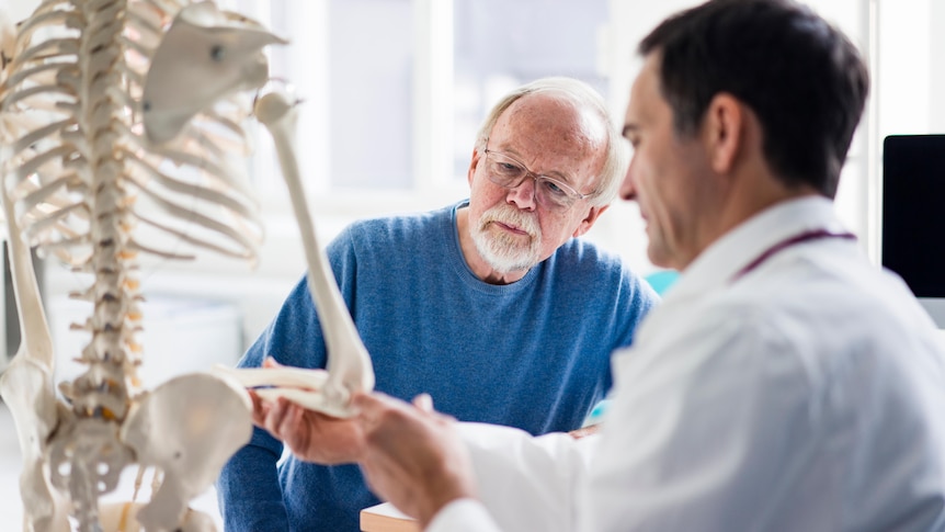 Doctor talking to older patient gesturing at a skeleton model