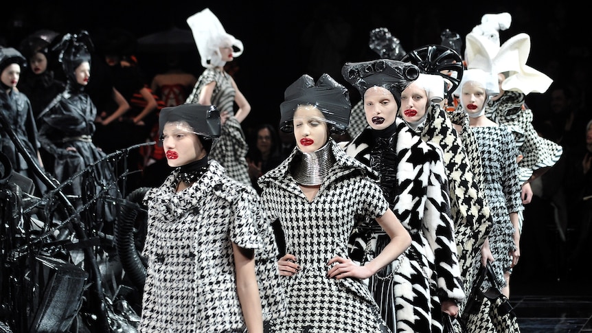 Models dressed in extravagant black-and-white tartan outfits and headpieces walk down a catwalk