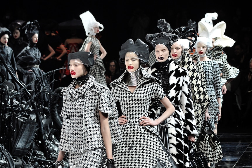 Models dressed in extravagant black-and-white tartan outfits and headpieces walk down a catwalk