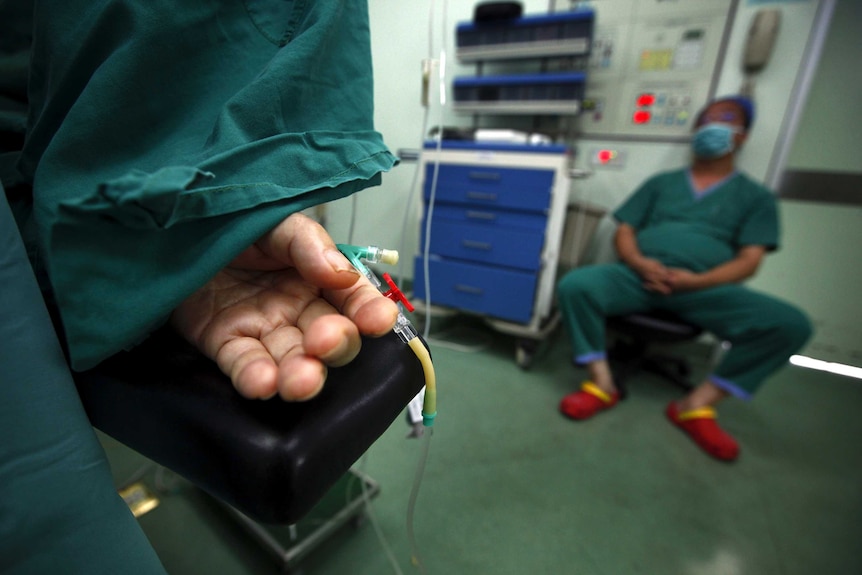 An anaethetist watches on as surgery is performed on a patient