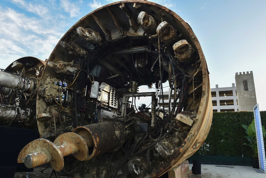 Muddy tunnel boring equipment sits above ground with blue skies overhead.