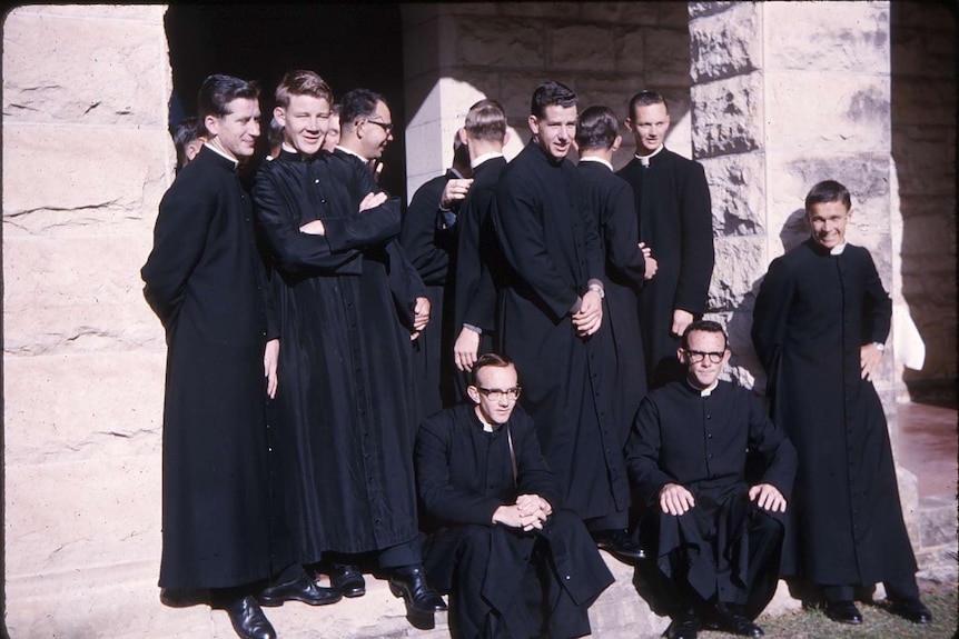 A black and white photo of trainee priests on the steps of a sandstone building.