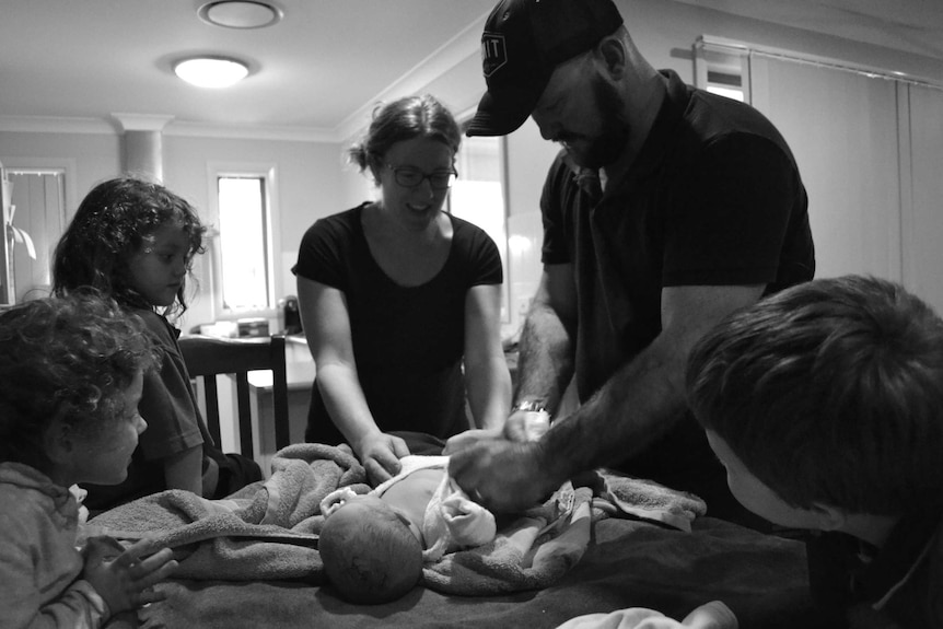 The Twidale family dresses newborn Memphis on the kitchen table.