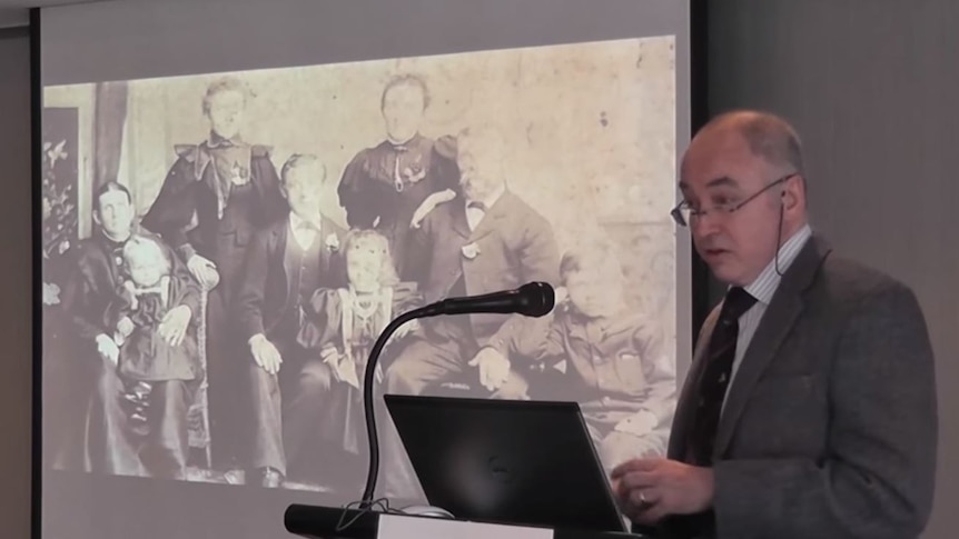 Man standing at a lectern giving a presentation on Huntington's disease