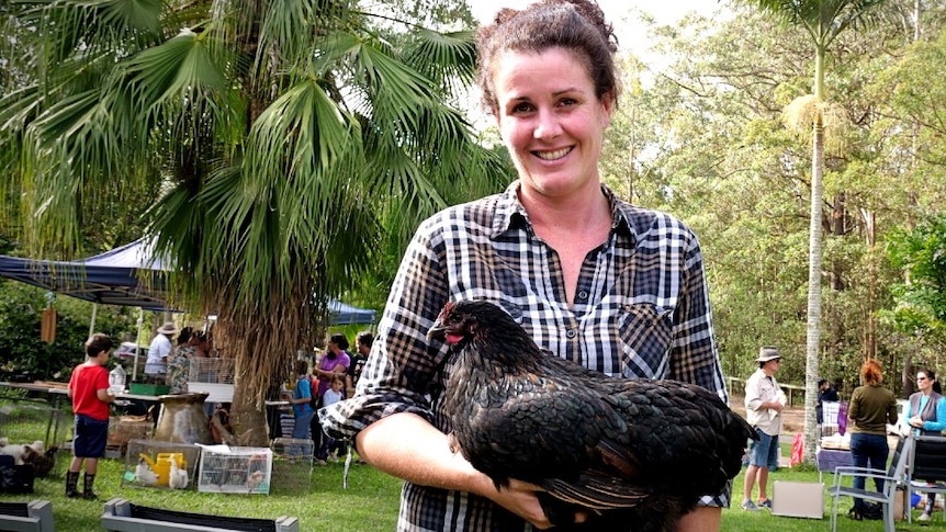 A woman stands in a  garden holding a chicken.