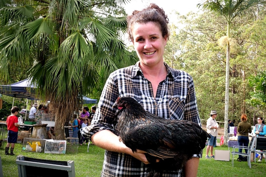 A woman stands in a  garden holding a chicken.
