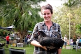 A woman stands in a  garden holding a chicken.
