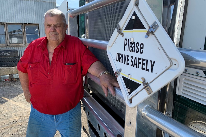 A man wearing a red shirt stands in front of a large truck.