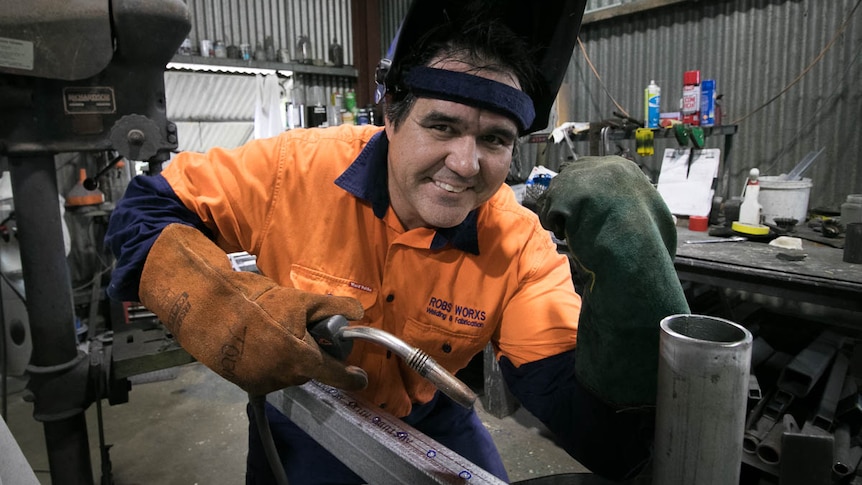 Man with welder and flexing arm in workshop.