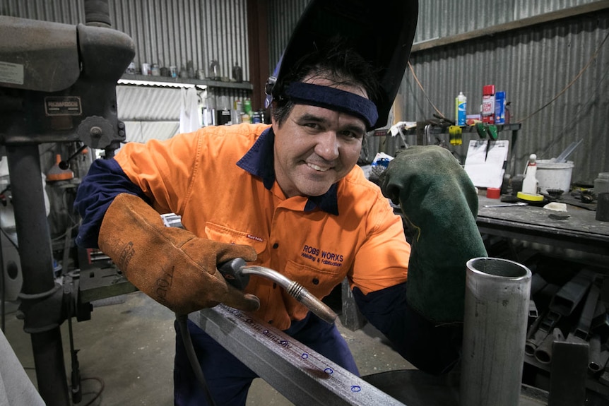 Man with welder and flexing arm in workshop.