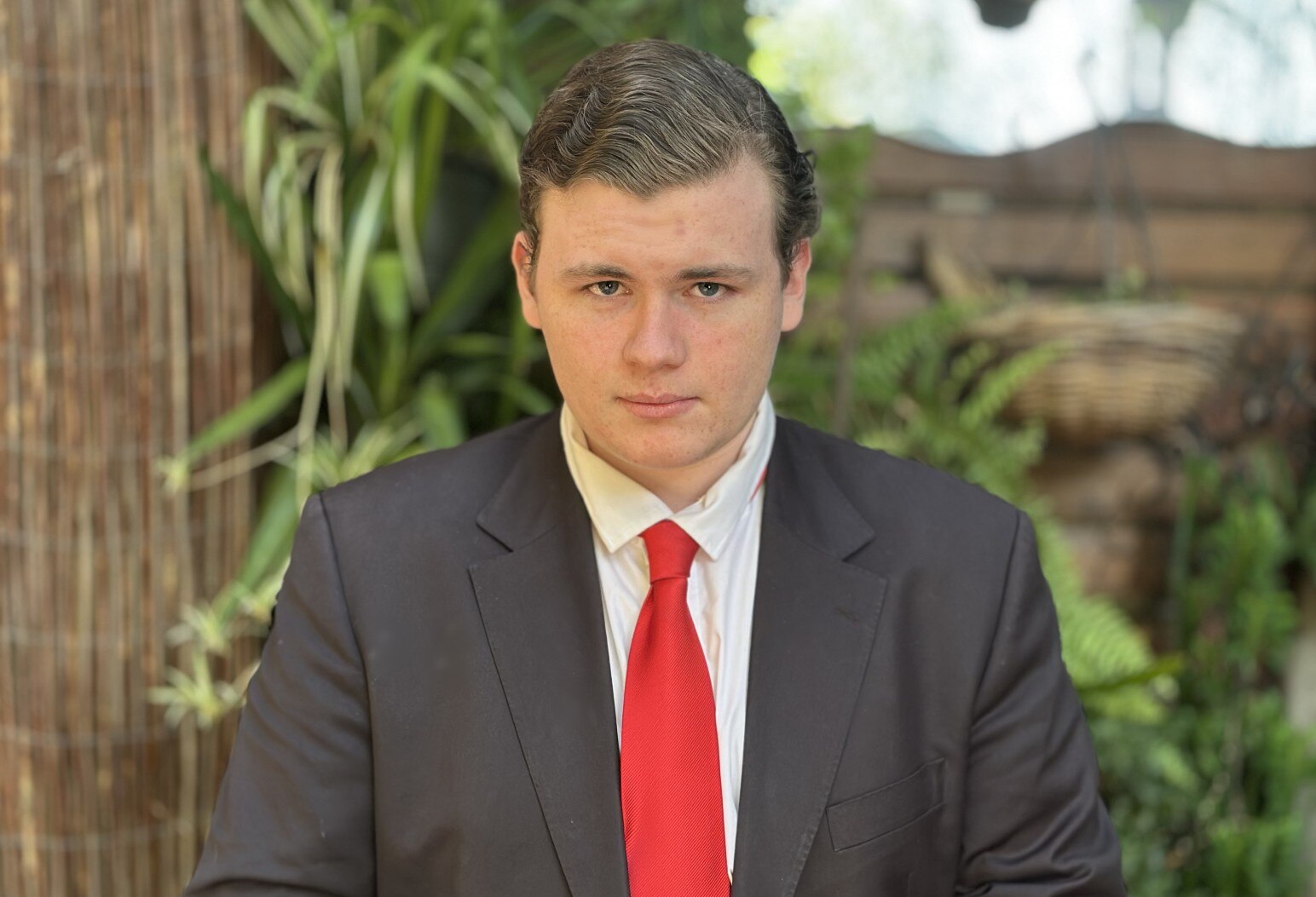 Leo, wearing a suit, looks at the camera with a serious expression. 