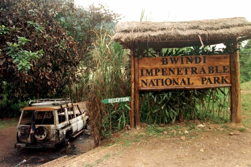 The husk of a 4x4 vehicle sits outside a large wooden sign for the Bwindi Impenetrable National Park