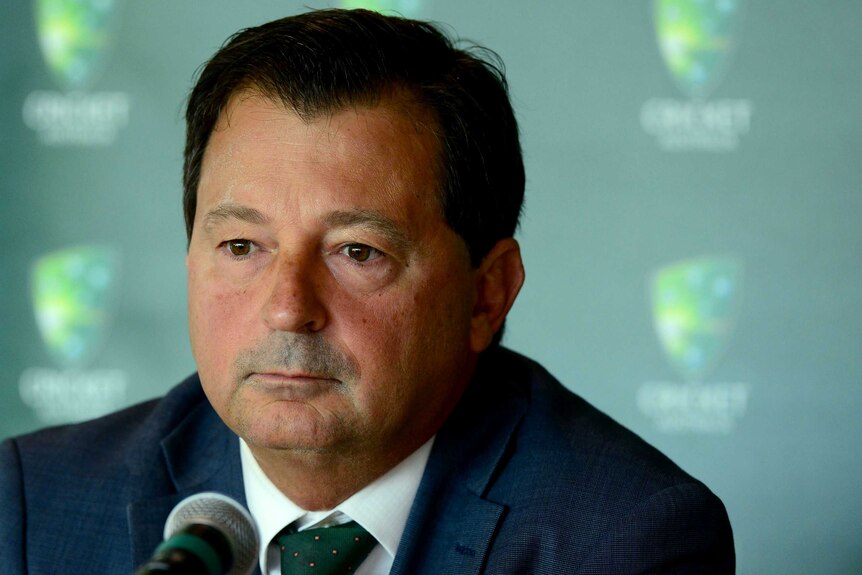 Cricket Australia chairman David Peever sitting behind a microphone at a media conference.