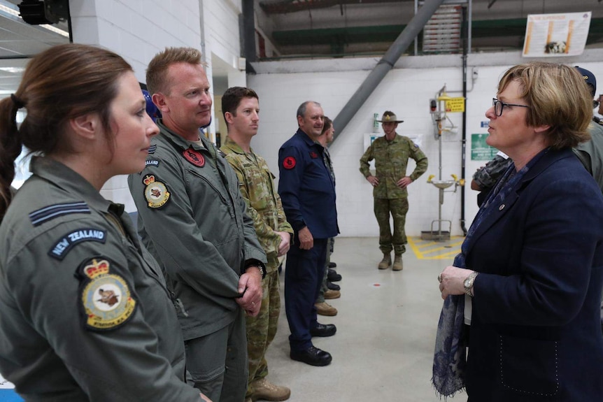 a man and woman in nz military uniform listen to a woman in a blazer and glasses speak to them as people watch on