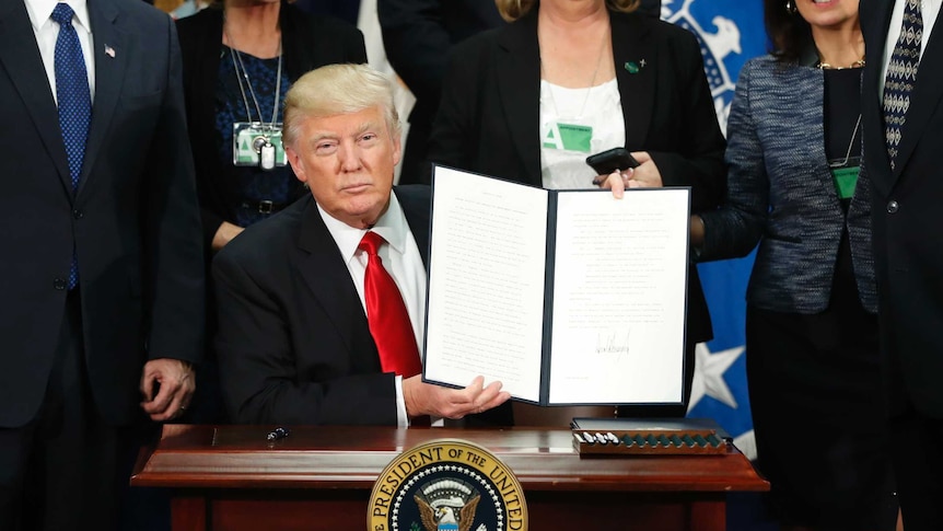 President Donald Trump, with Vice President Mike Pence, holds up an executive order on the Mexico border wall, January 25, 2017.