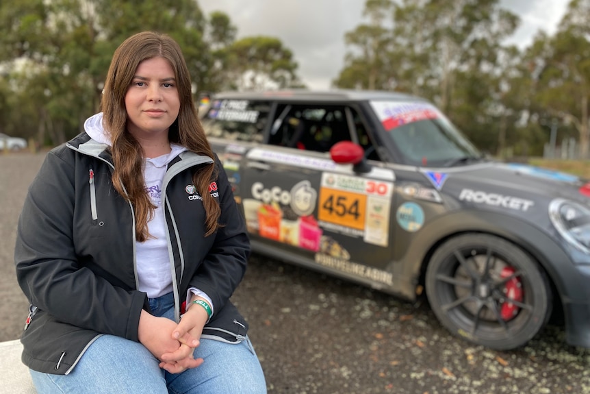 Casey Price sits in front of her car, looking serious.