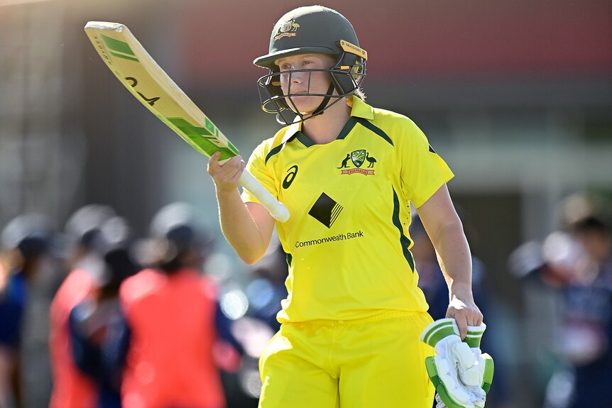 An Australia female cricketer raises her bat after being dismissed against India.