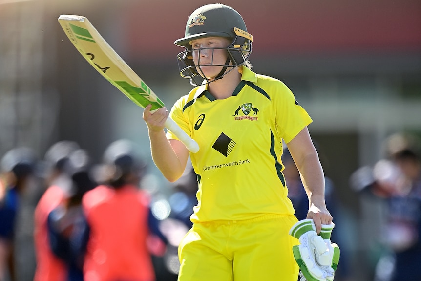 An Australia female cricketer raises her bat after being dismissed against India.