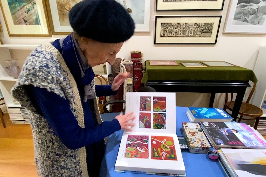 An elderly woman well dressed flipping pages of an art book inside a small gallery