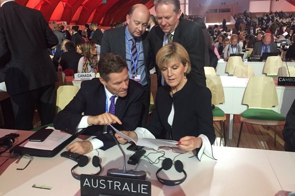Julie Bishop sits at a table surrounded by other officials reading a paper document.