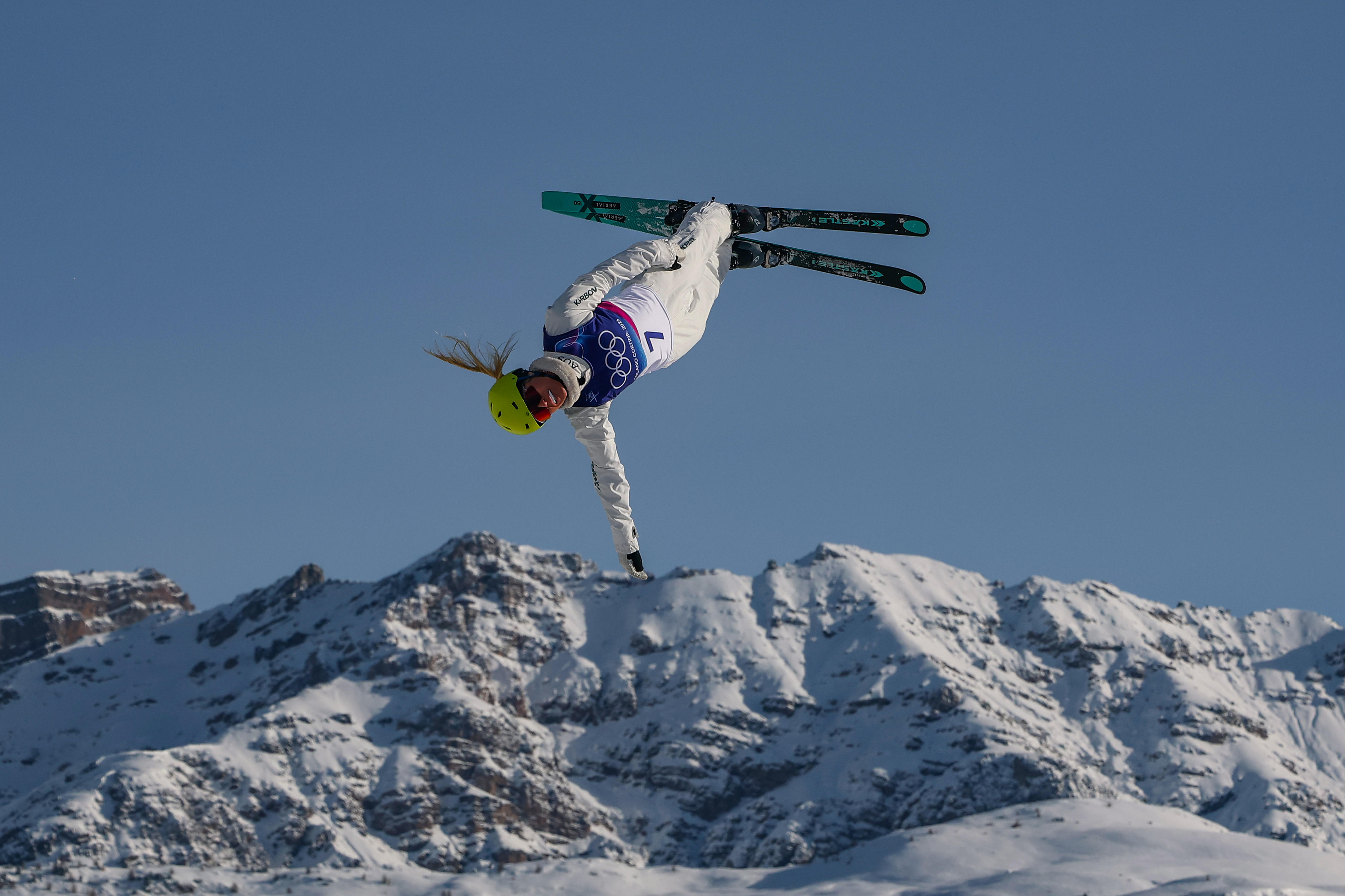 Uma esquiadora olímpica realiza uma manobra aérea em um cenário alpino.