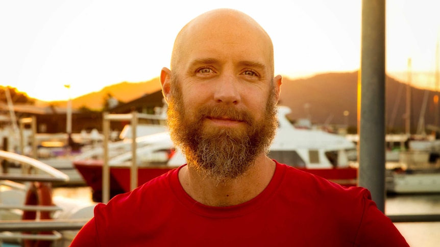 Eddie Game stands on a pier with boats in the background