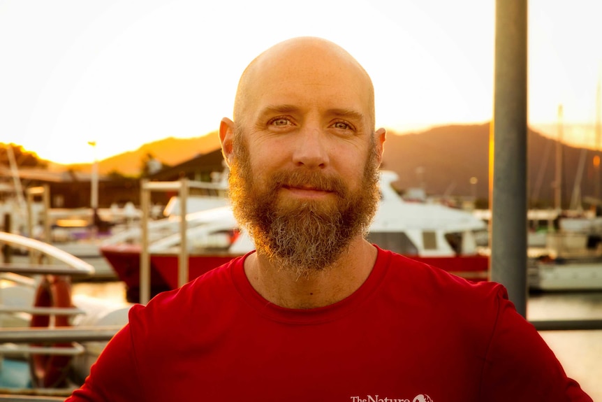 Eddie Game stands on a pier with boats in the background