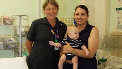 A woman standing next to a young mother in a hospital room who is holding a baby aged around 3 months