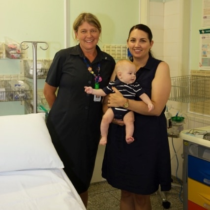 A woman standing next to a young mother in a hospital room who is holding a baby aged around 3 months