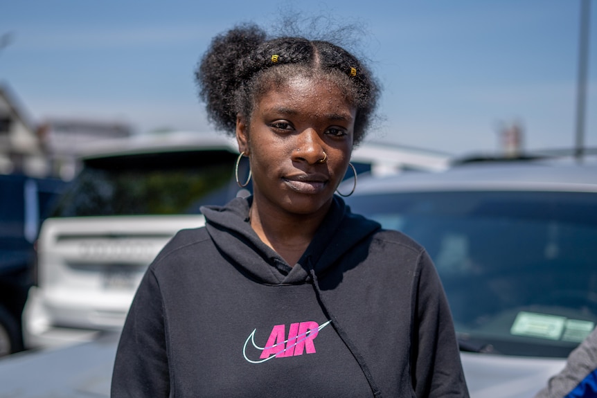 African American woman standing alone wearing black hooded jumper and silver hoop earrings