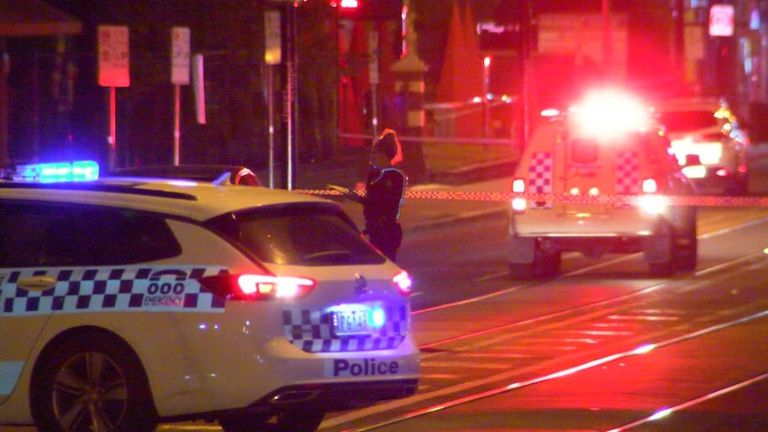 A police officer stands near two police cars, which are emitting blue and red lights at night.