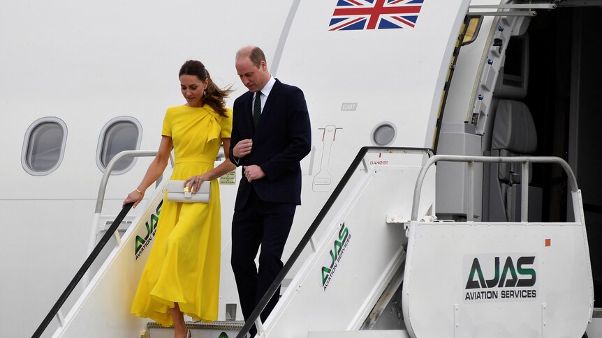 The duke and duchess of cambridge walk down a set of plane stairs. the duchess is wearing a bright yellow dress