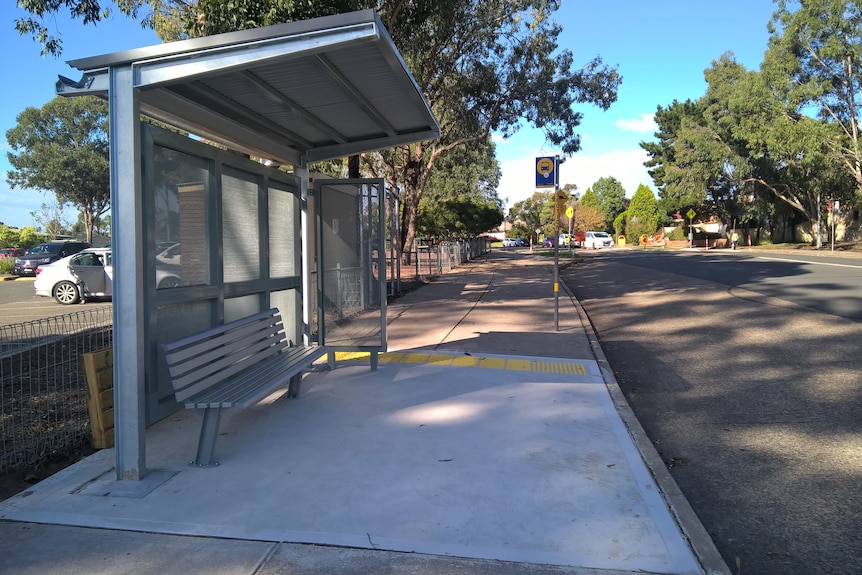 A shaded silver bus shelter on the left hand side of a road