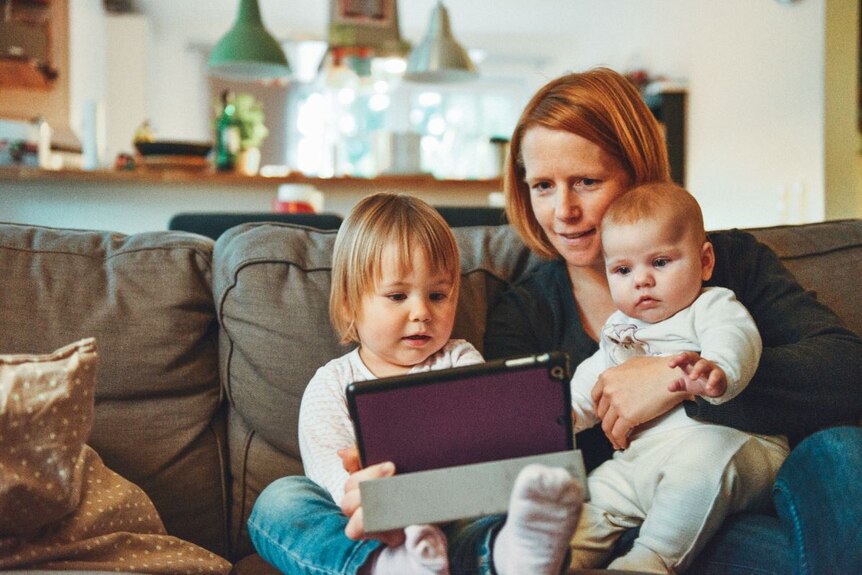 A woman and two young children look at a tablet.