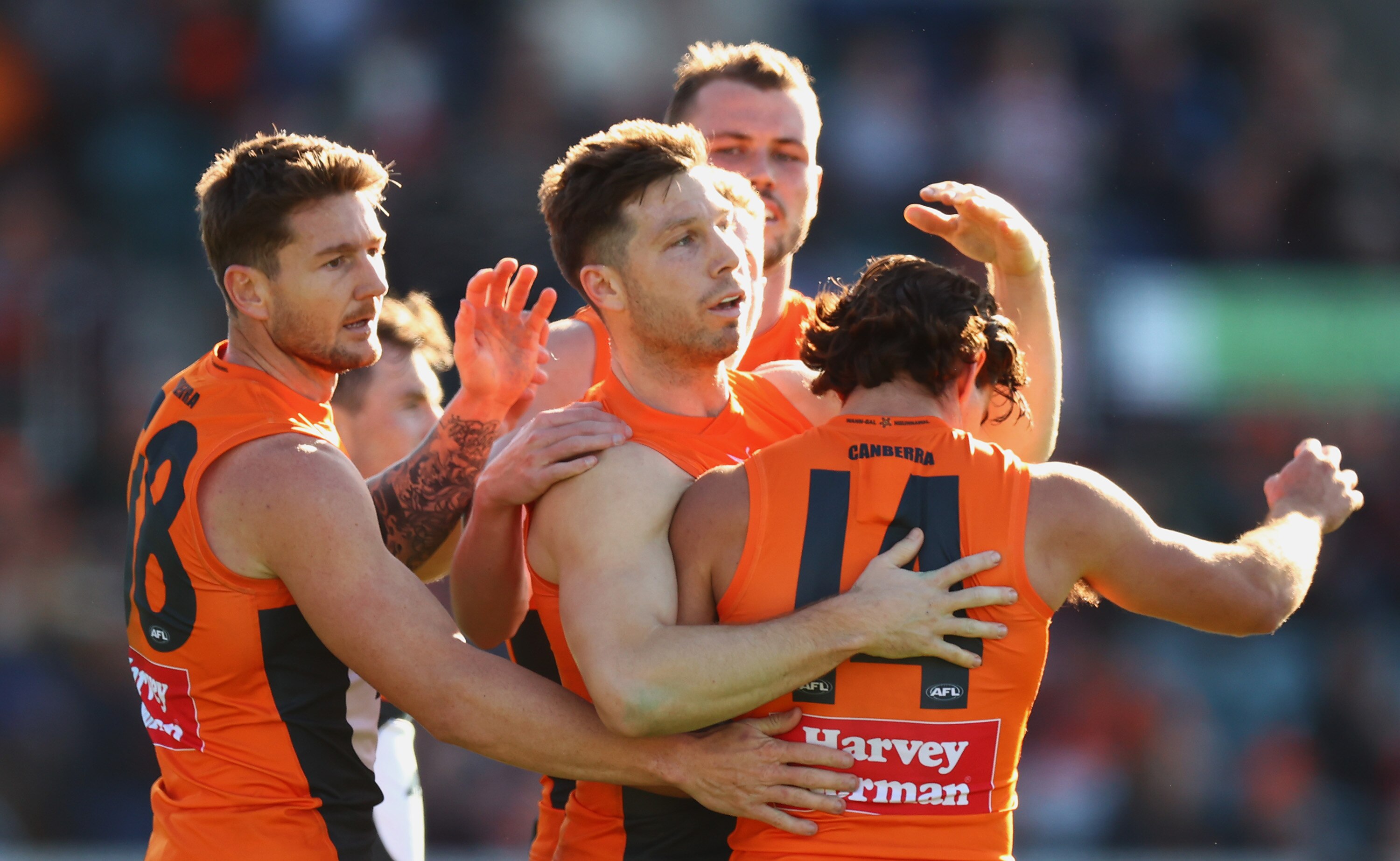 A group of GWS AFL players embrace as they celebrate a goal against Gold Coast Suns.