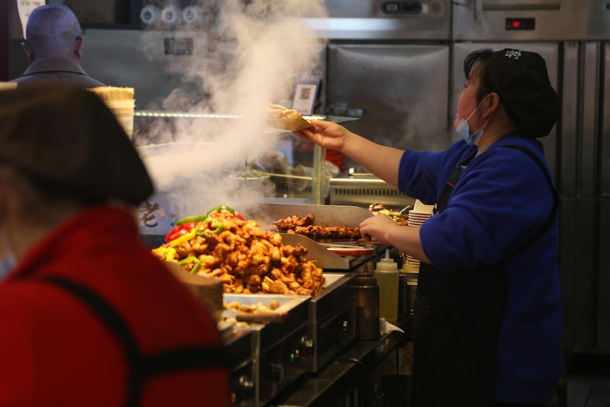 A woman checks on a piece of food cooking on a stove.