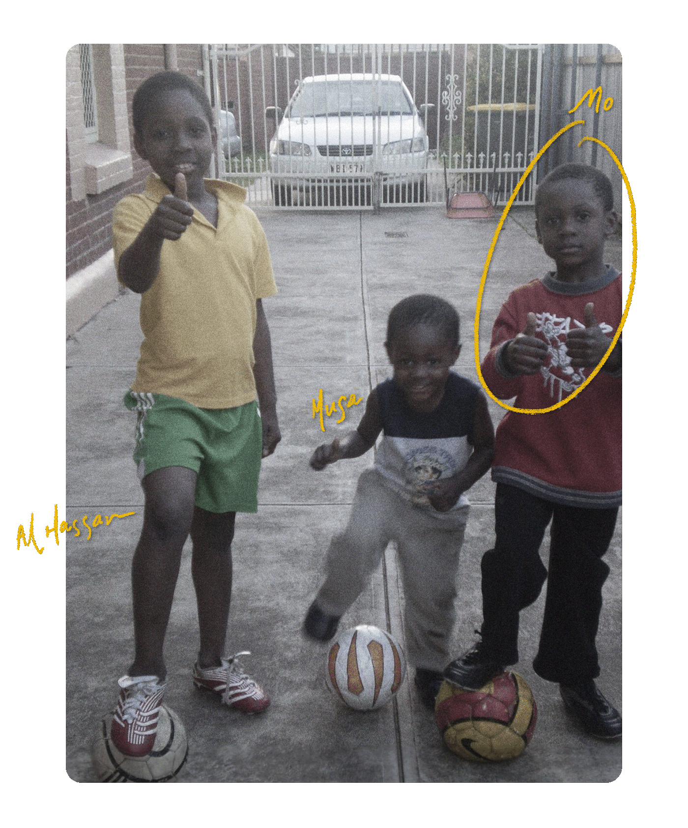 Low quality colour photograph of three children standing in driveway with one foot on soccer balls.