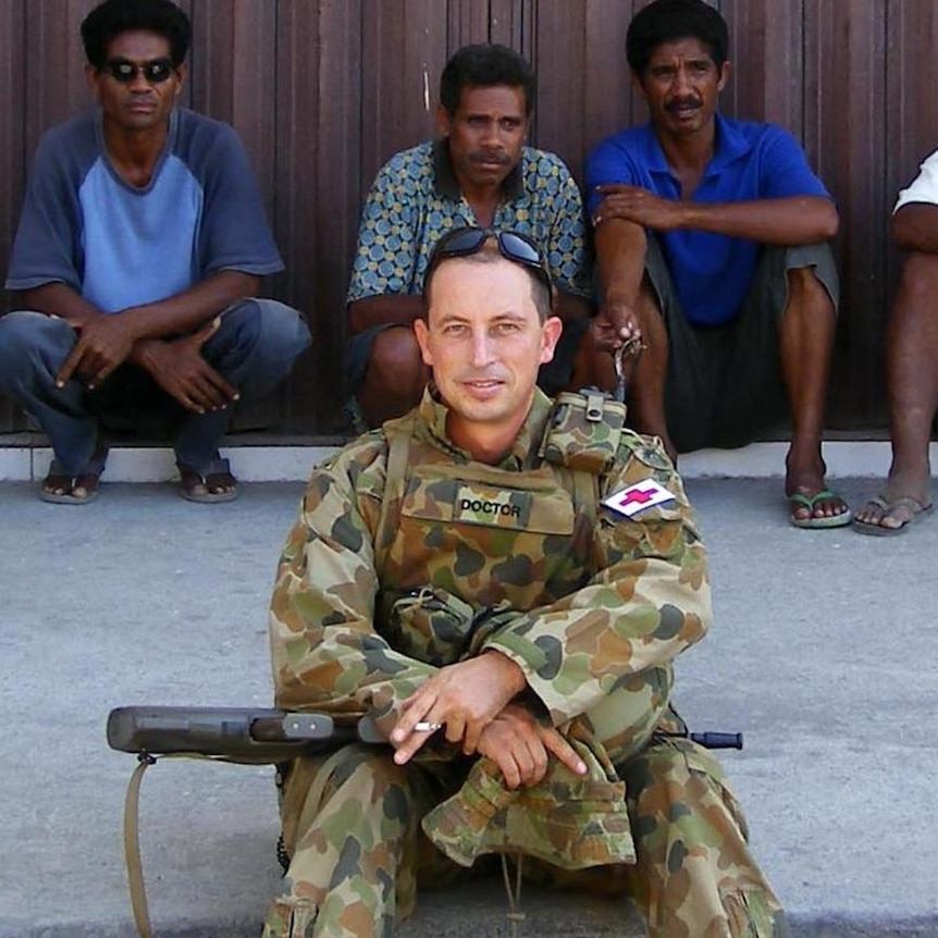 Dr Julian Fidge sits by the side of the road, wearing army fatigues while on duty in East Timor.