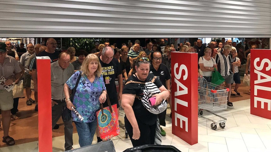 Shoppers walk under a roller door to get into a shopping centre with sales signs.