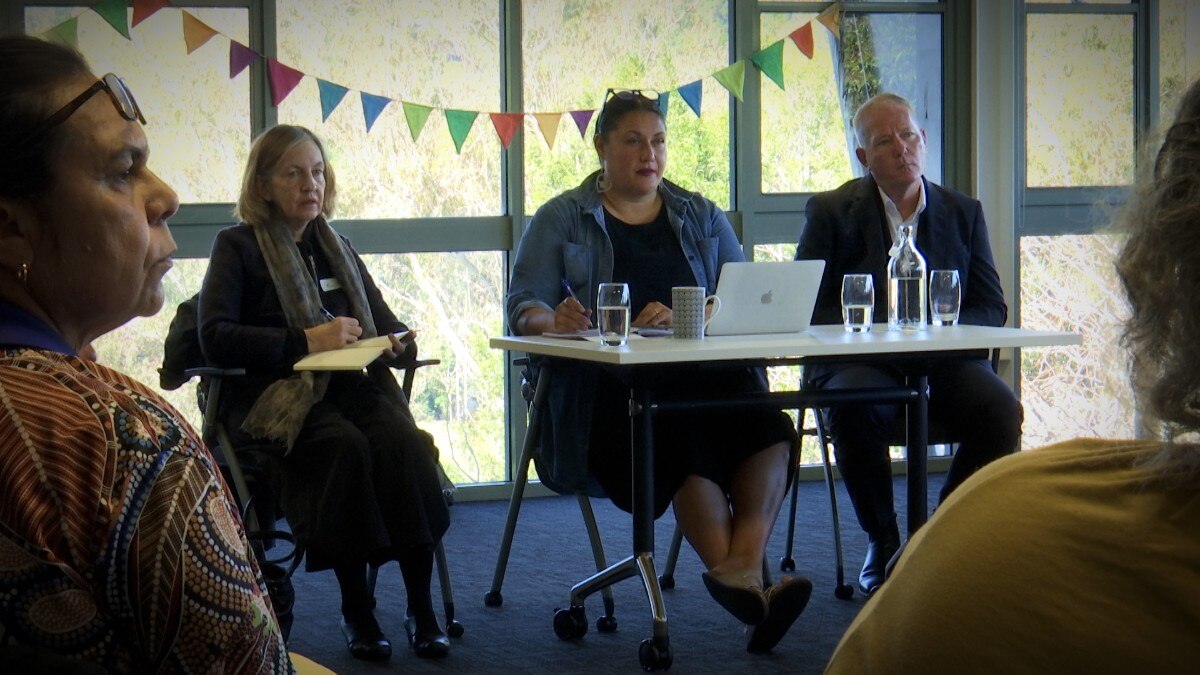 Three people sitting with notebooks in a room with big glass windows